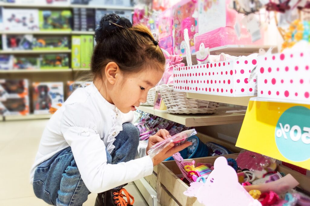 Asian child girl chooses toys on the shelves of a toy store, makes purchases in children's stores.