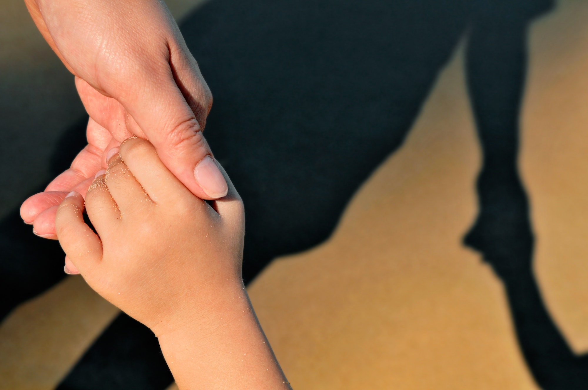 Closeup of mother and child holding hands with their shadow in brown sand background.