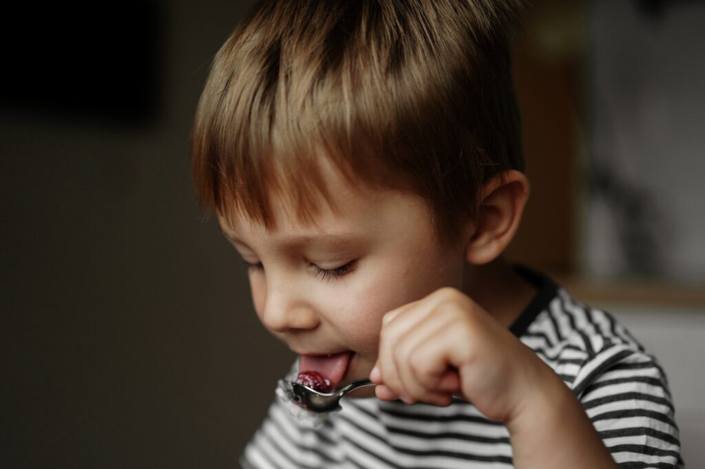 Cute little boy tasting raspberry with tip of his tongue