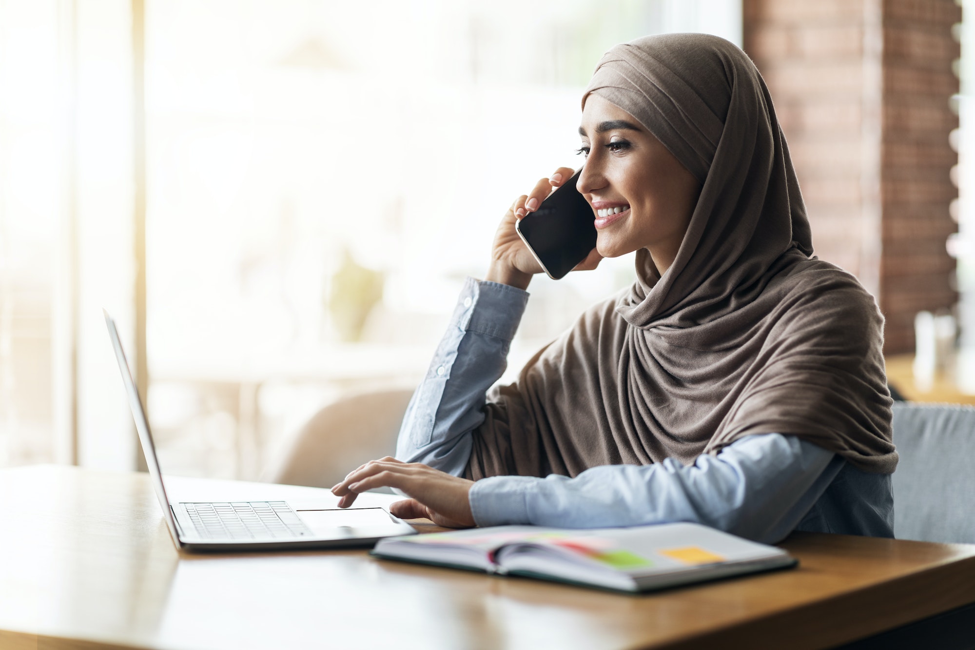 Girl in hijab looking for job online, talking on phone