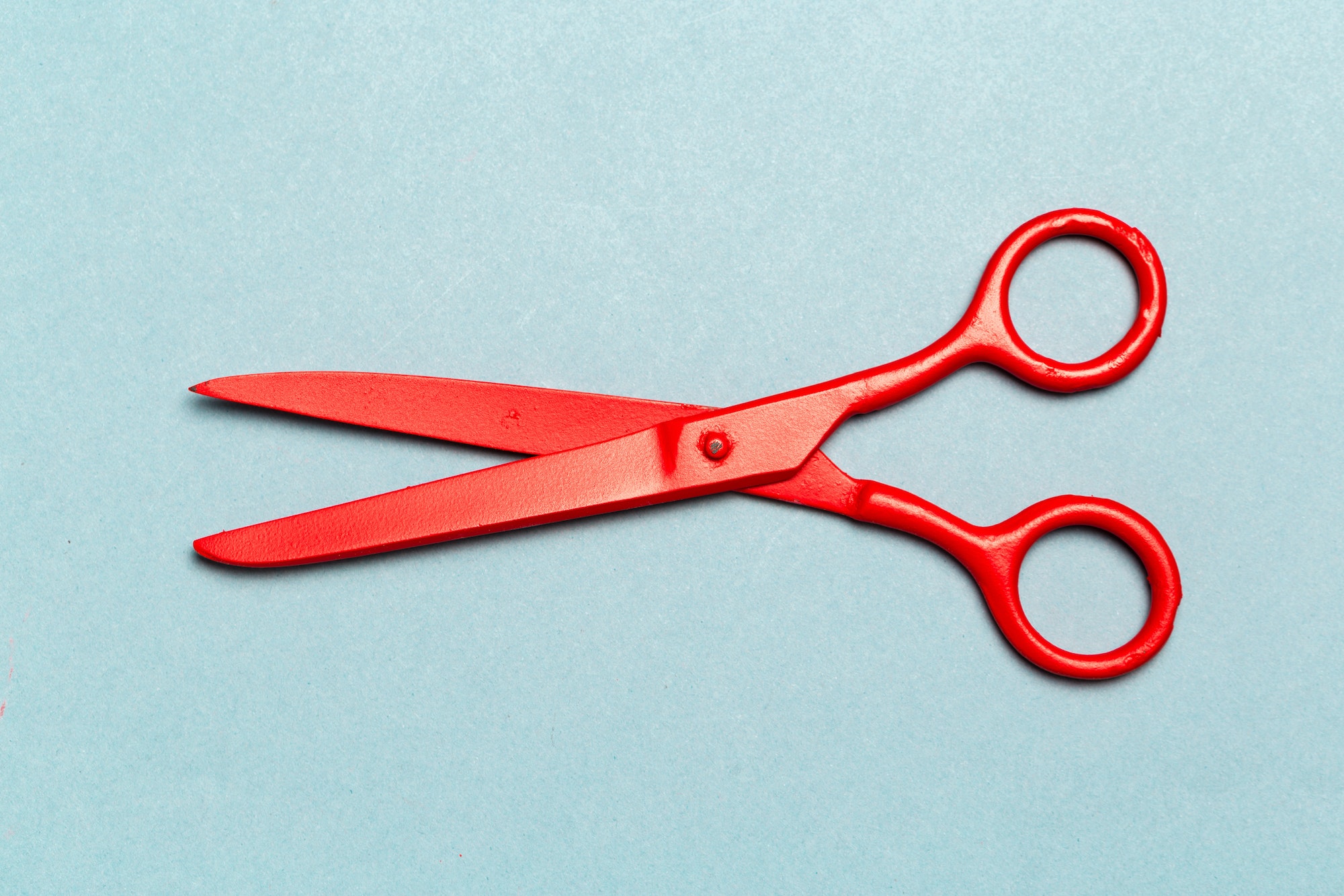 Red scissors on light blue background close up
