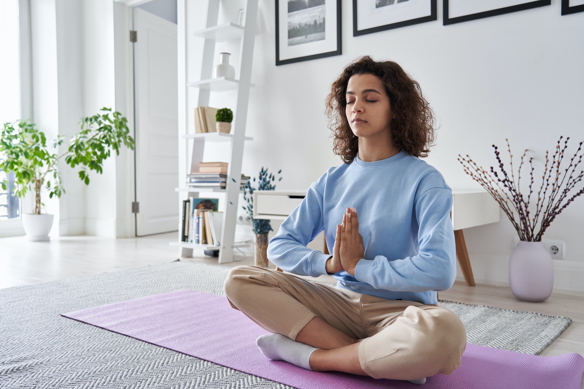 Serene healthy young woman meditating at home doing yoga breathing exercise.