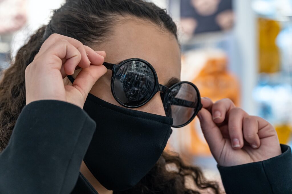 Shallow focus closeup of a female wearing sunglasses and a mask inside the clothes shop