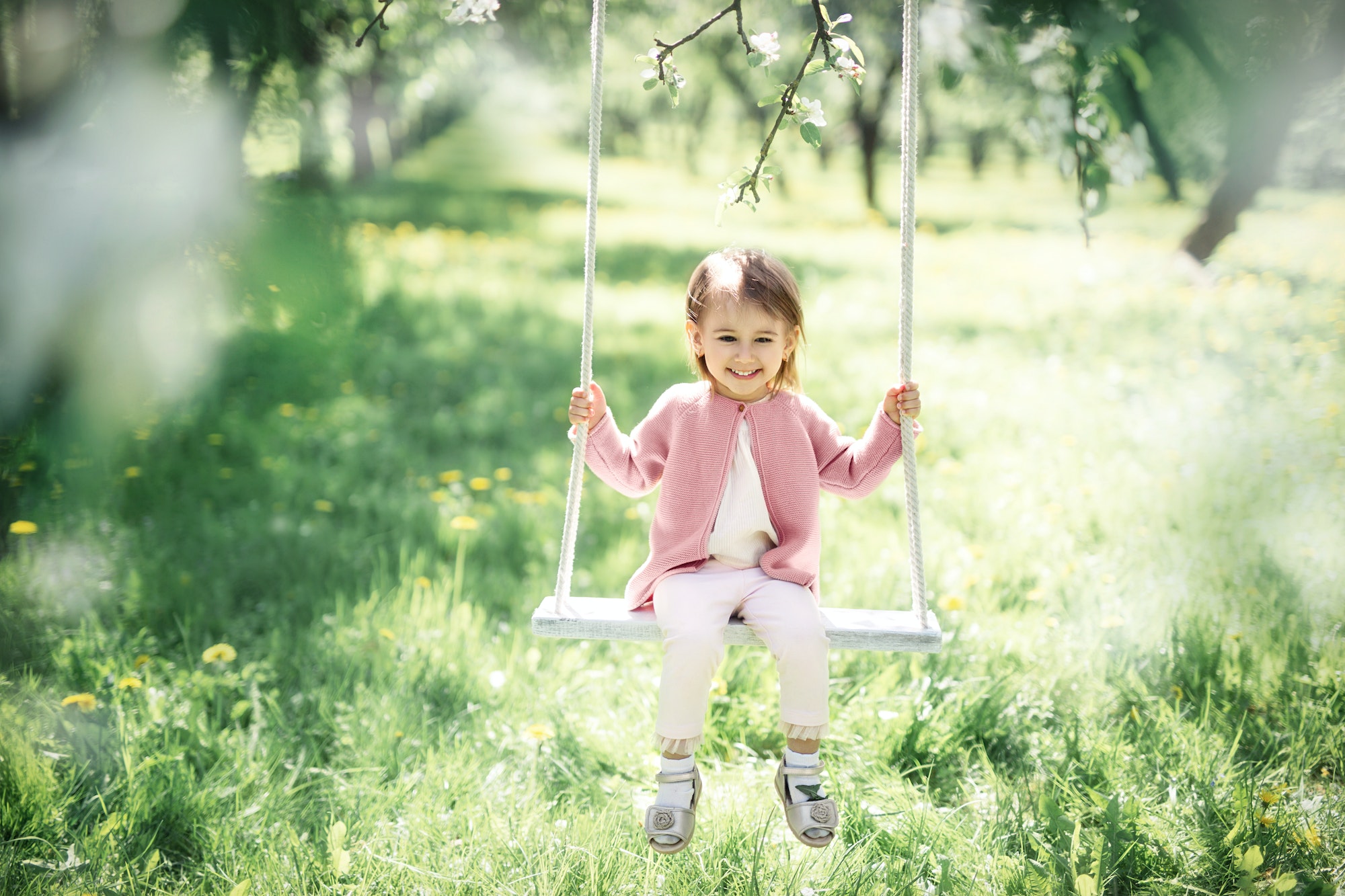 A little girl is swinging on a swing in a blooming garden.