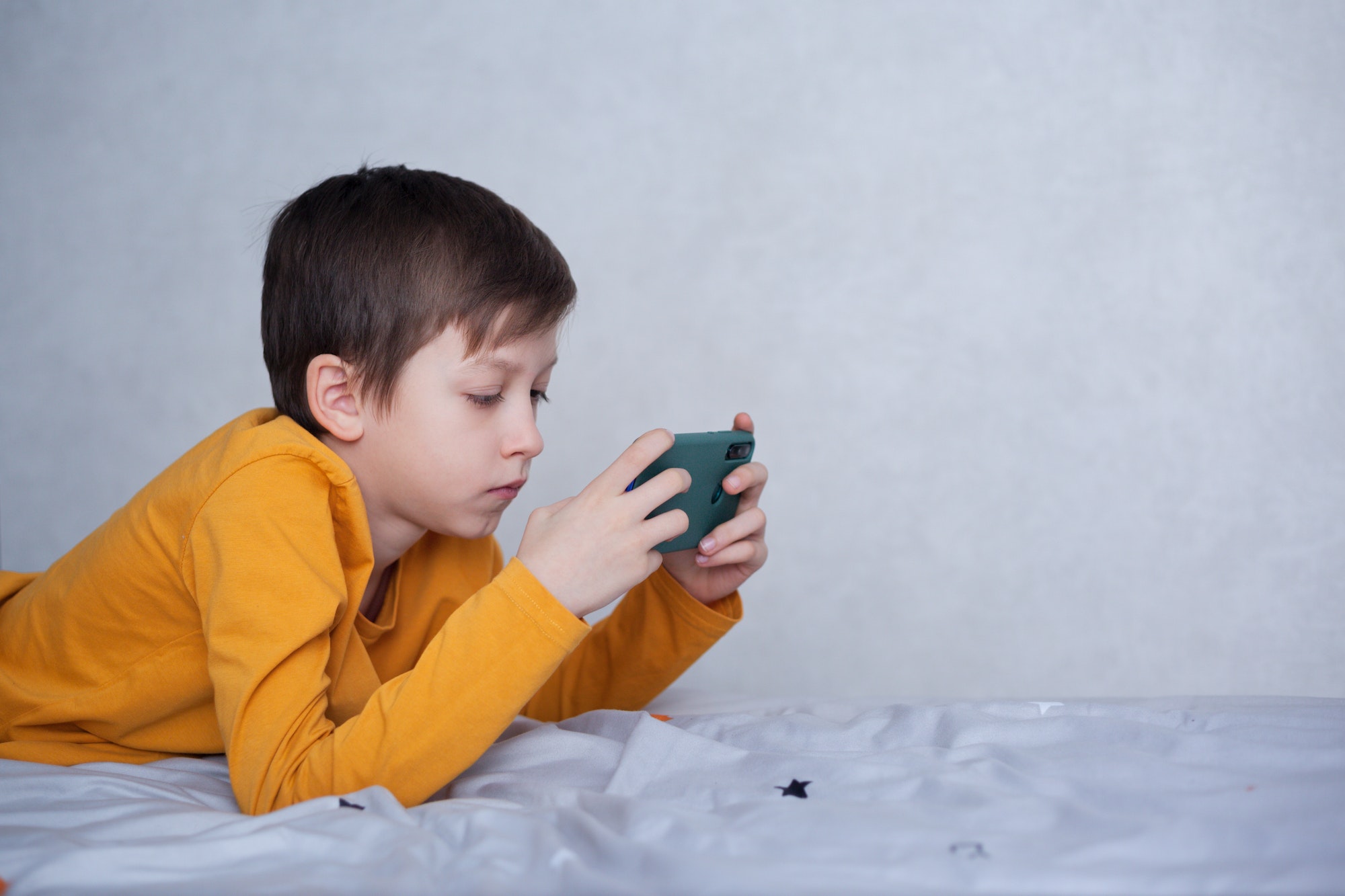 Cute little kid boy plays in video game on his smartphone. Child has fun playing videogame.